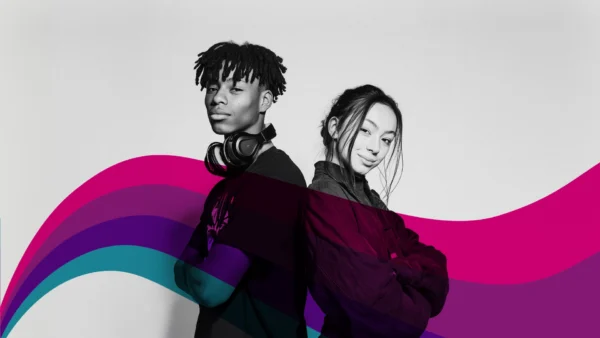 Two individuals standing back‑to‑back in a studio setting, both with arms crossed. A flowing wave pattern in pink, purple, and teal curves across the lower part of the image.