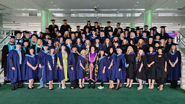 A large group of graduates dressed in academic gowns and caps standing together on an indoor staircase for a formal group photo.
