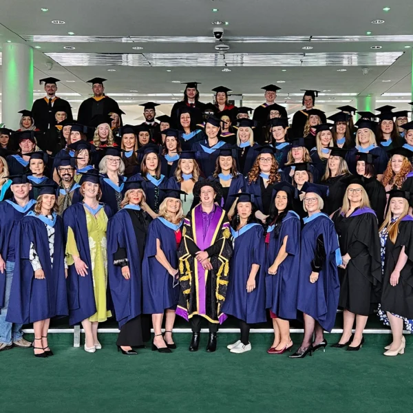 A large group of graduates dressed in academic gowns and caps standing together on an indoor staircase for a formal group photo.