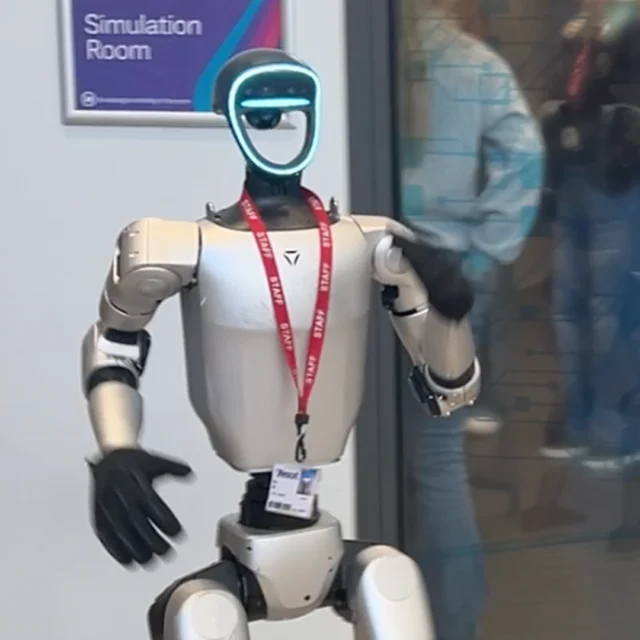 Humanoid robots standing outside a simulator room with it's hands raised.
