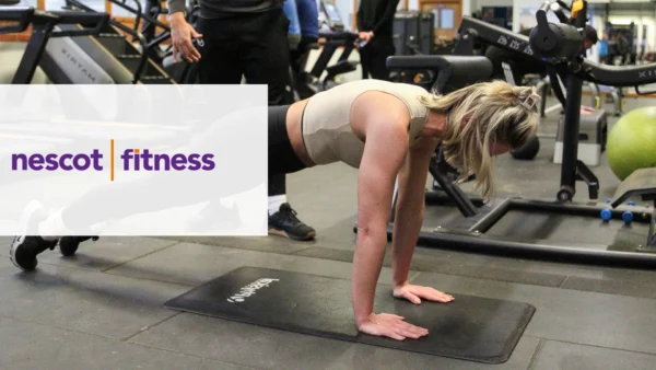 A person performing a plank exercise on a mat in a gym, surrounded by workout equipment. The Nescot Fitness logo is displayed on the left side of the image.