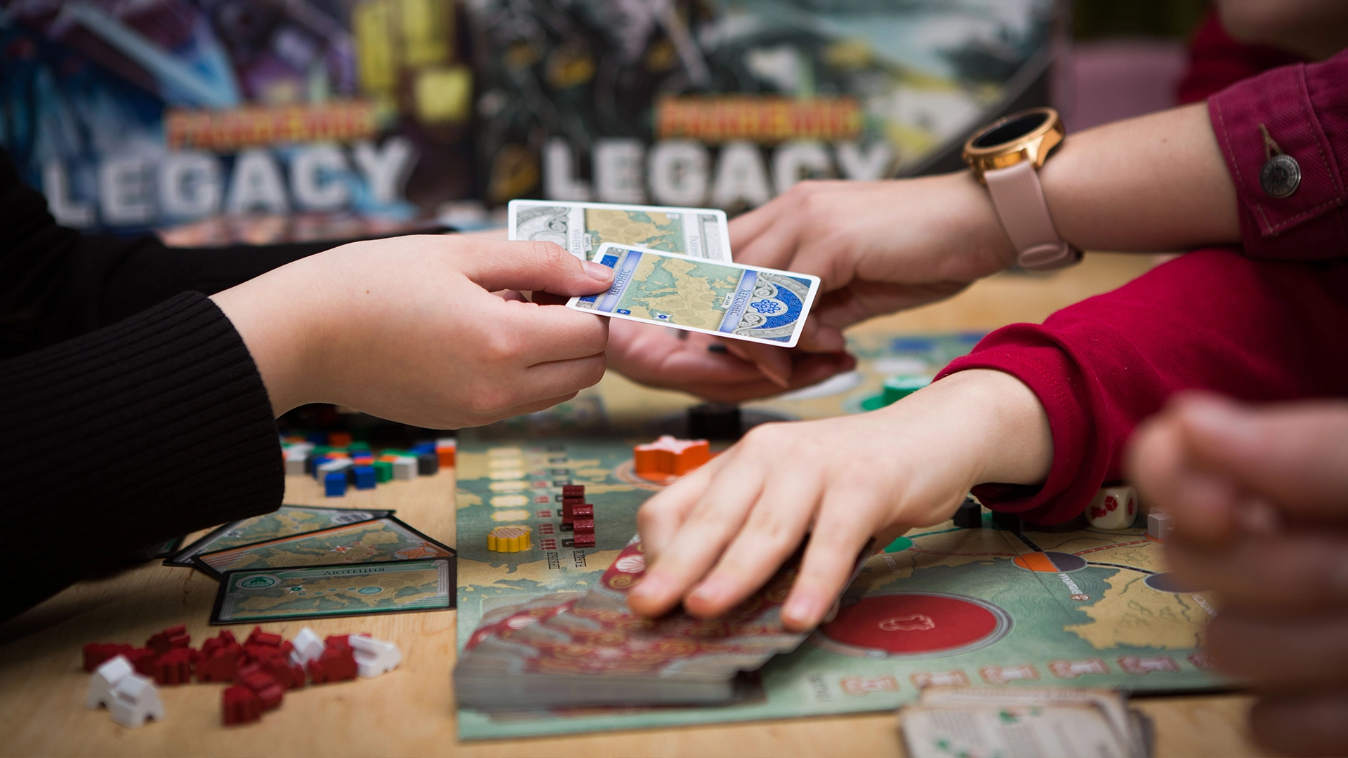 Close-up of several hands passing cards and moving pieces on a tabletop during a board game.