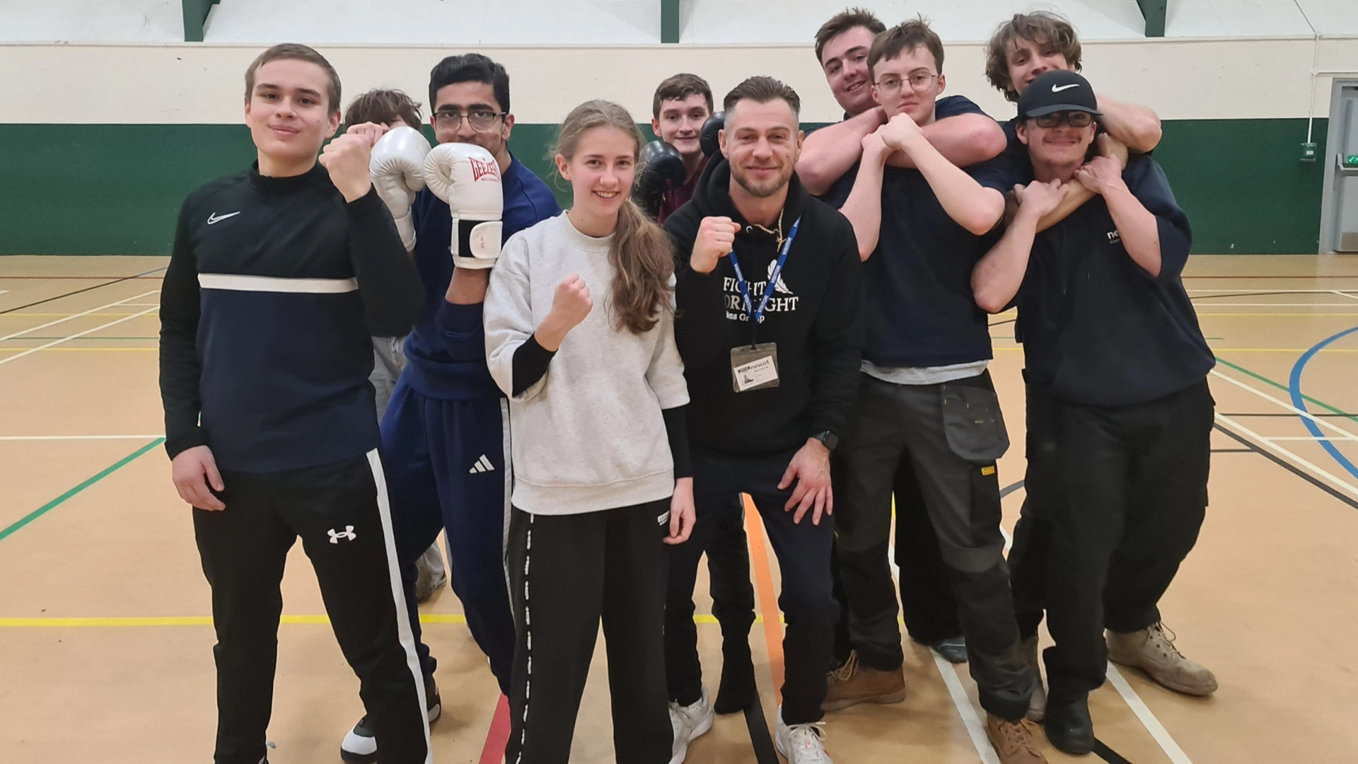 Group of people standing together in a sports hall, some wearing boxing gloves, posing for a group photo.