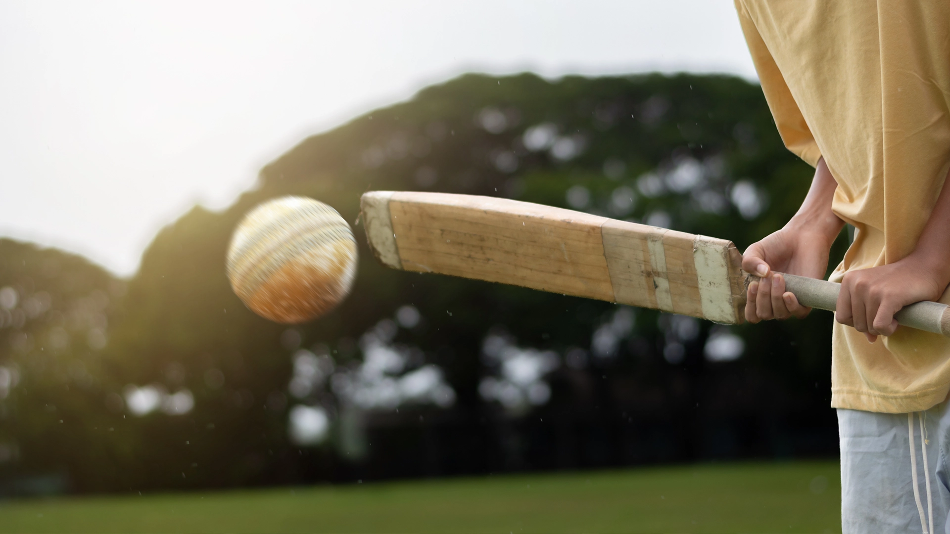 Close-up of a person holding a cricket bat and striking a moving ball on an outdoor field.