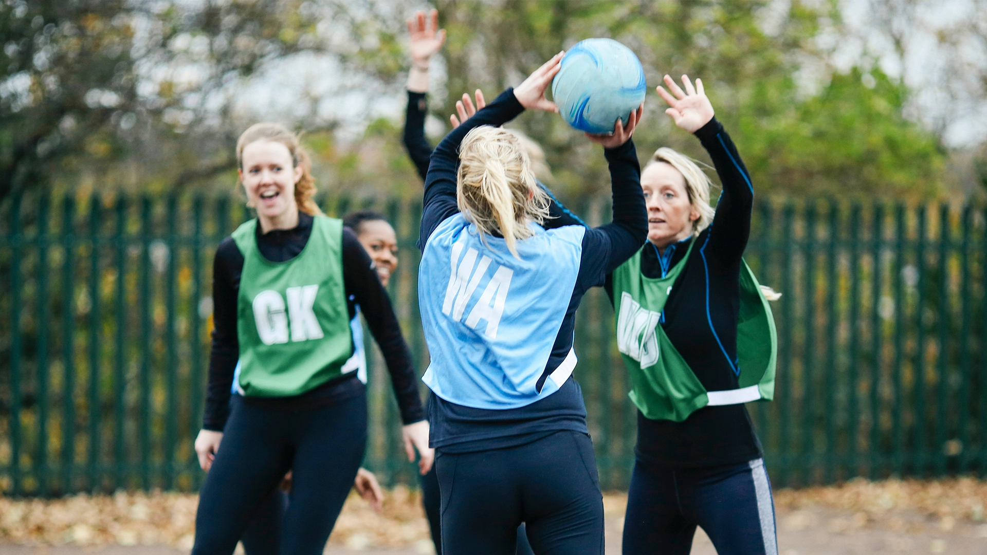Players wearing green and blue bibs actively competing for the ball during an outdoor netball game.