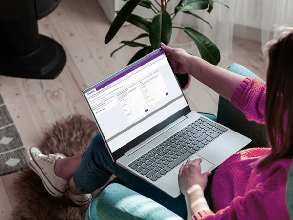 A person seated indoors using a laptop displaying online bursary portal, with the device resting on their lap in a home-style setting.