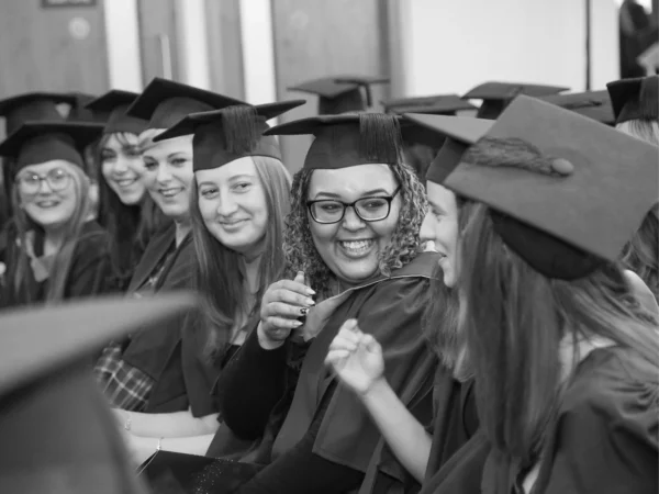 Nescot students wearing graduation gowns and mortarboards seated together at a college graduation ceremony.