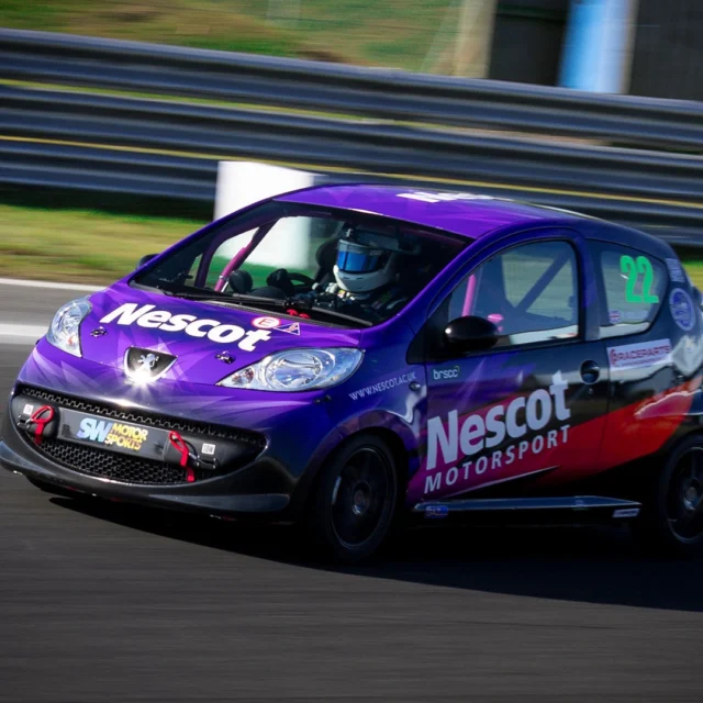 Purple Nescot Motorsport race car, number 22, driven on a track with motion blur in the background.