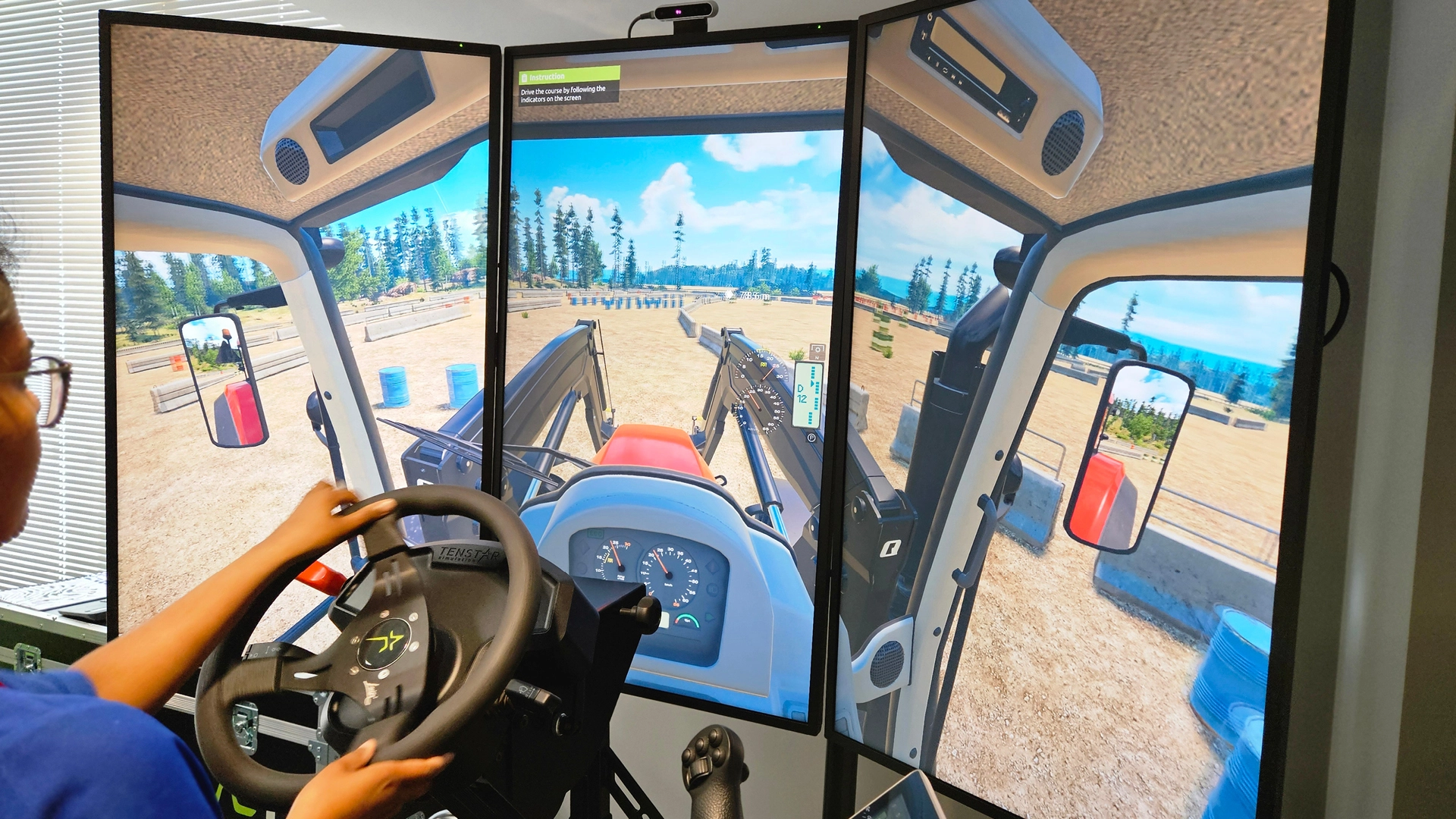 A person uses a multi-screen driving simulator, steering a virtual vehicle displayed across three monitors in a training environment.