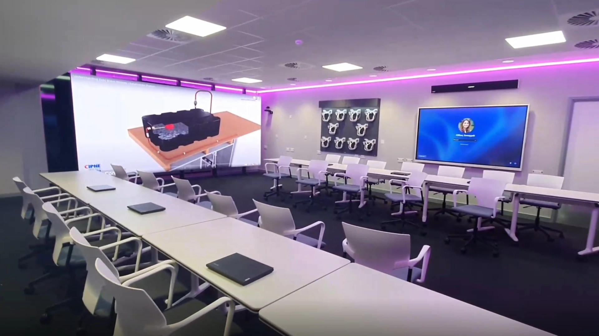 A contemporary teaching space with rows of desks and wheeled chairs, featuring large wall-mounted screens and ambient LED lighting for presentations and collaborative learning.