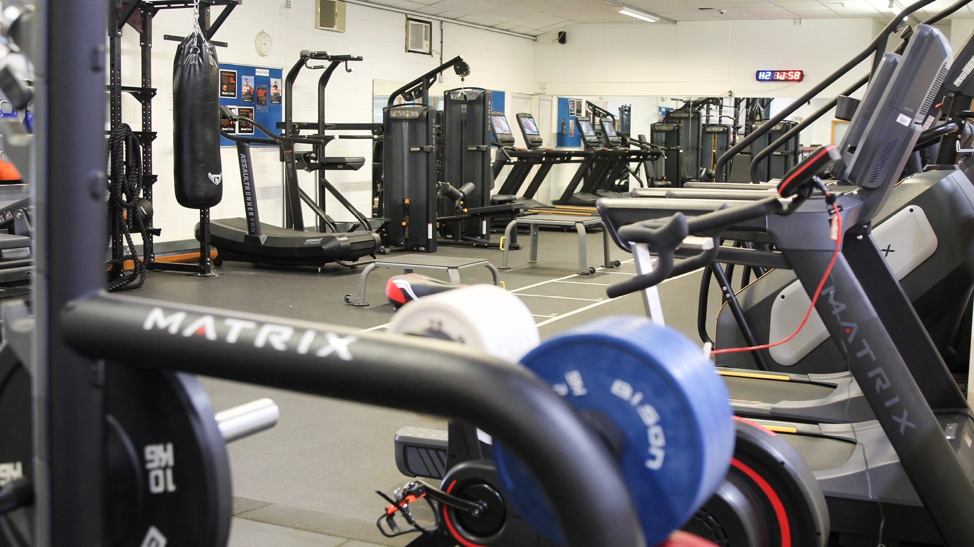 A modern college gym featuring treadmills, exercise bikes, weight machines and a punching bag, laid out across a clean indoor fitness area.