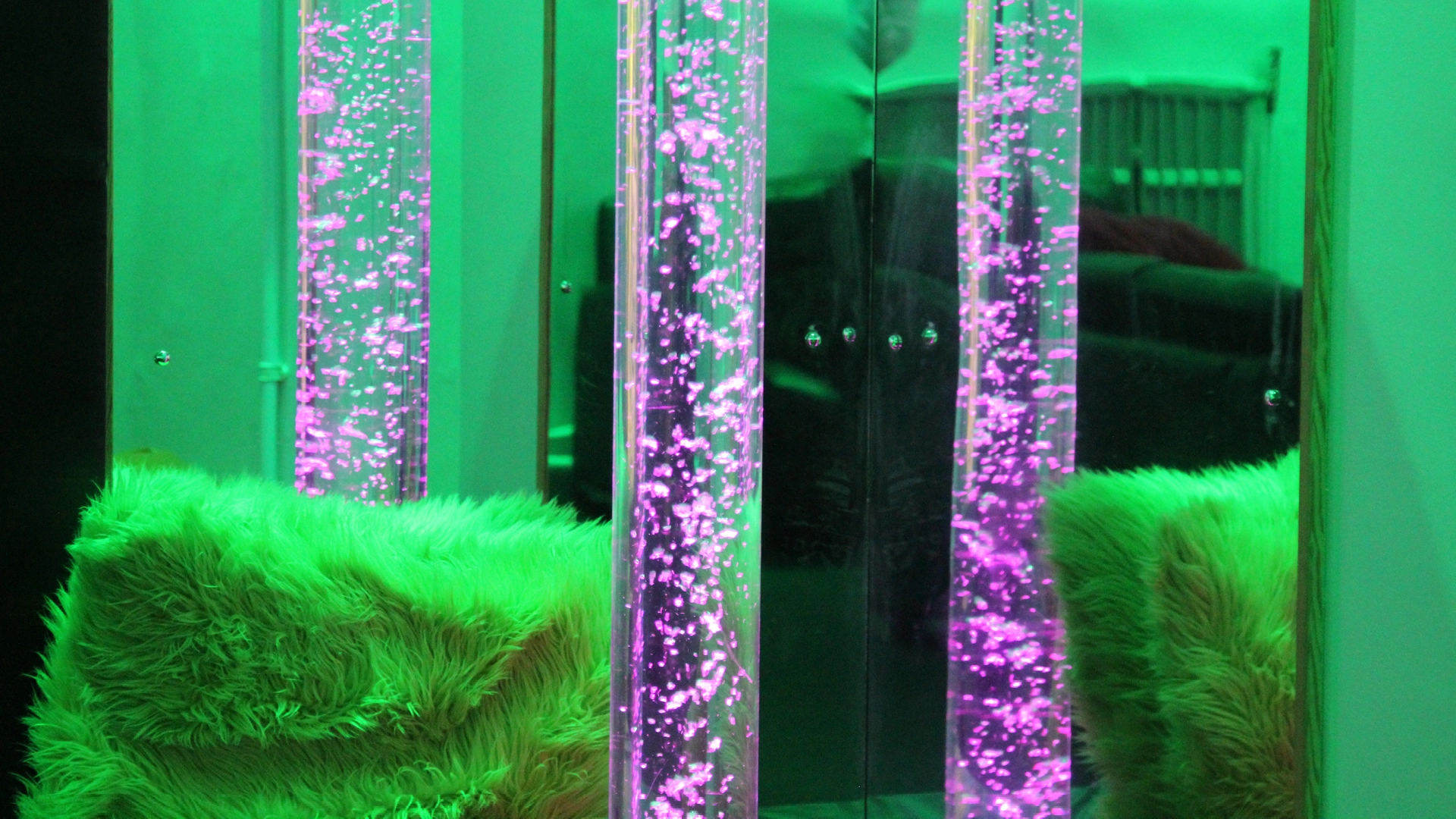 Sensory bubble tubes glowing pink and green beside a soft seating area.