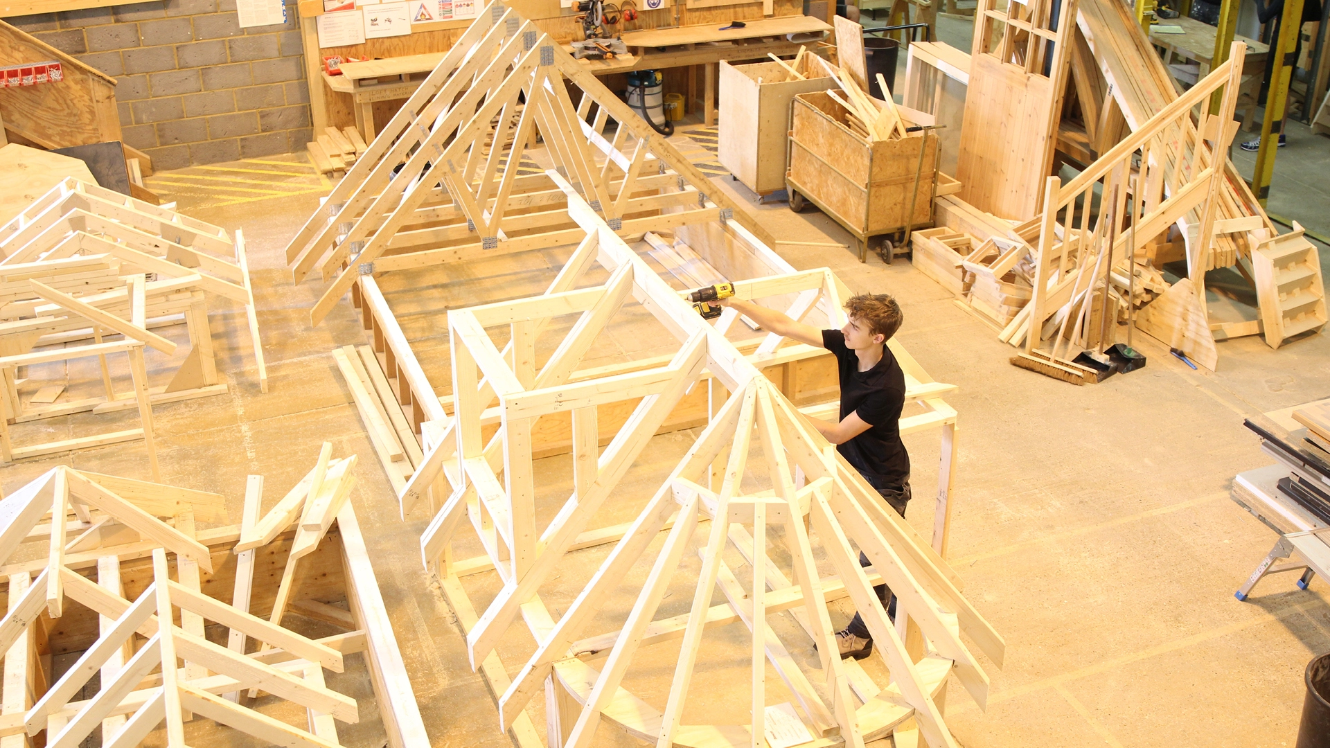 Nescot student assembling a wooden roof frame in a construction workshop.