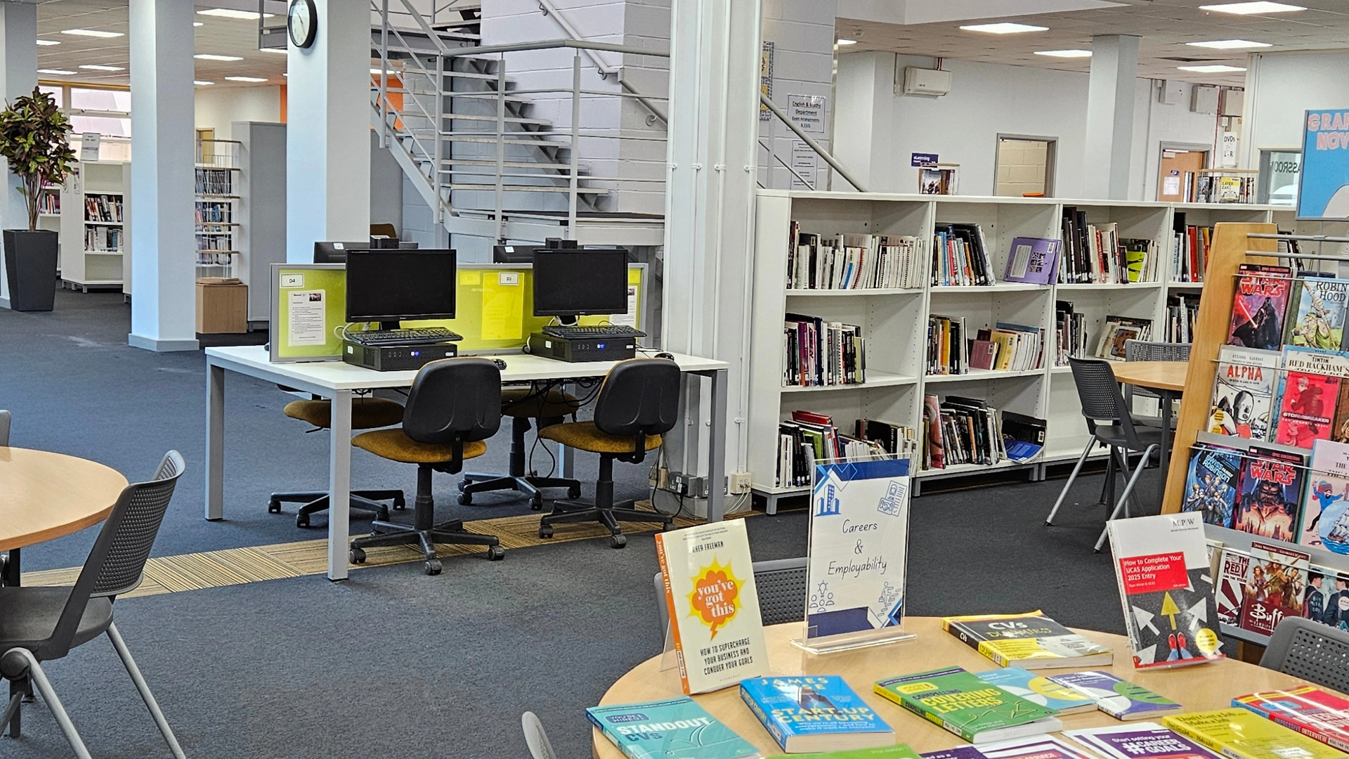 Nescot library with computers, bookcases and study tables, including a display of careers and study skills books in the foreground.