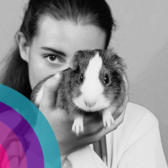 Person holding a guinea pig close to the camera in a black and white portrait.