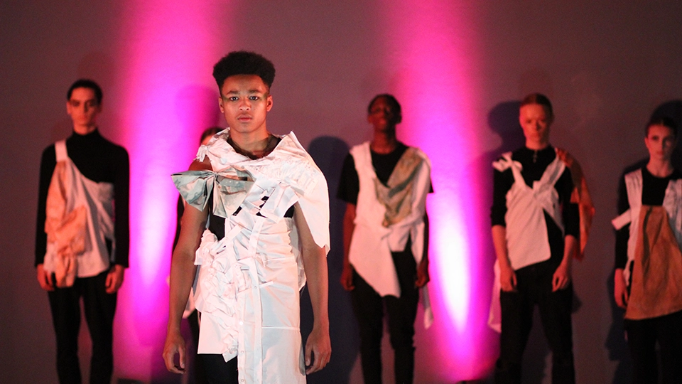Student modelling a handmade garment under green lighting, with others blurred in the background.