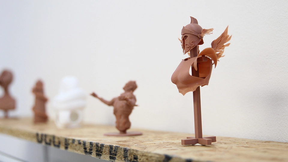 Row of small 3D‑printed sculptures displayed on a wooden shelf against a plain wall.