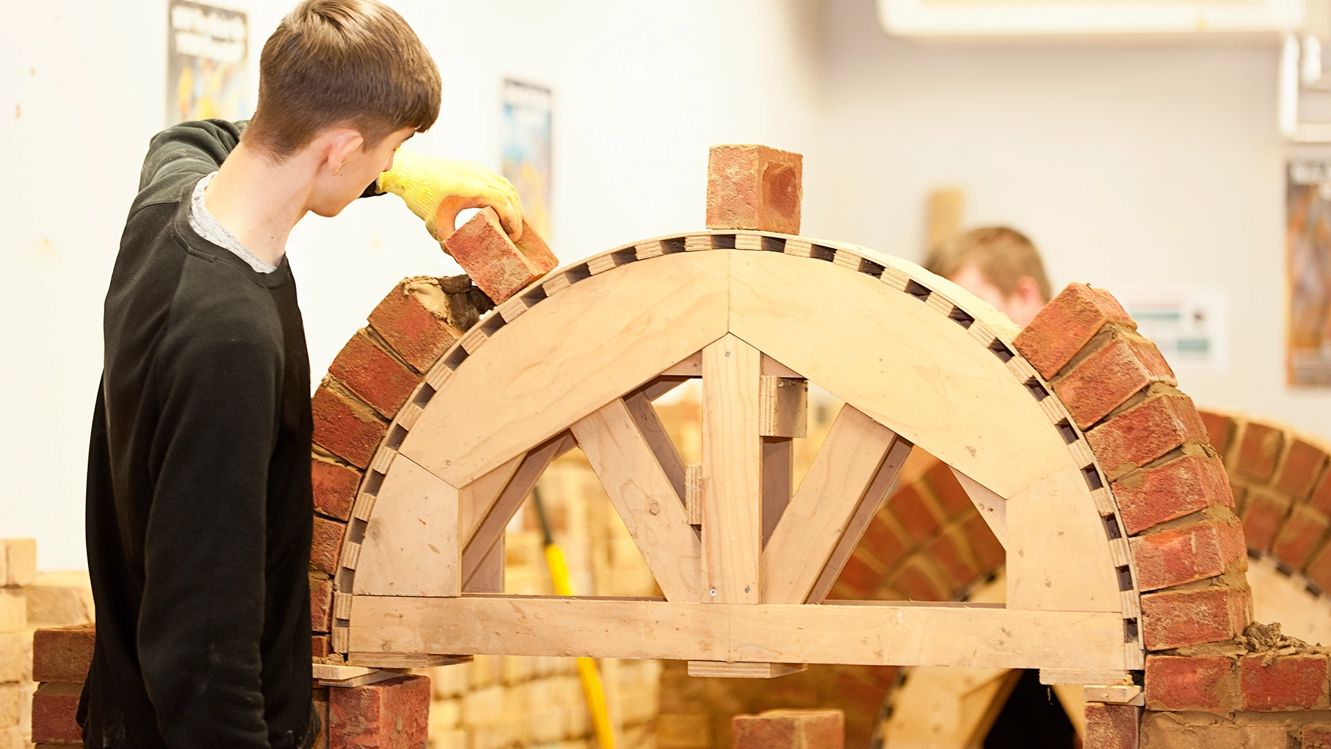Person placing bricks to form an arch on a wooden support frame.