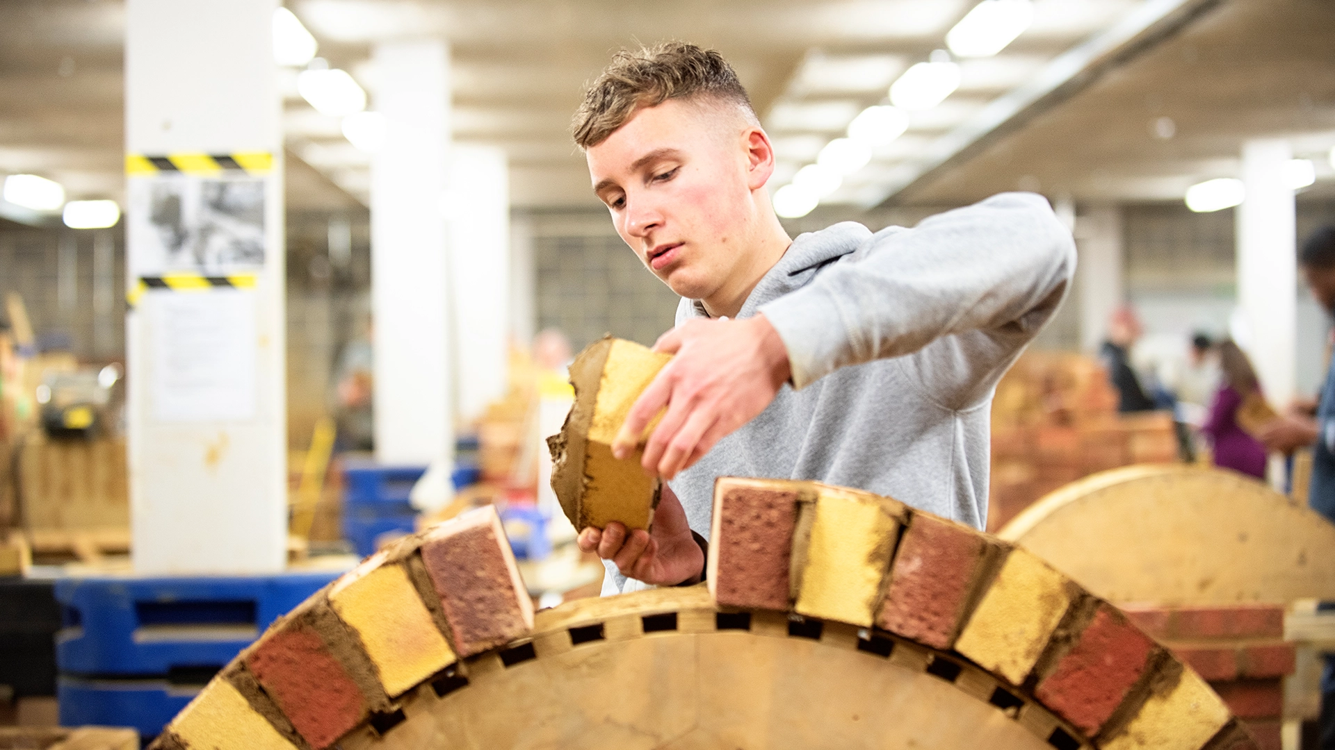 Person positioning a brick on a curved arch structure in a workshop.