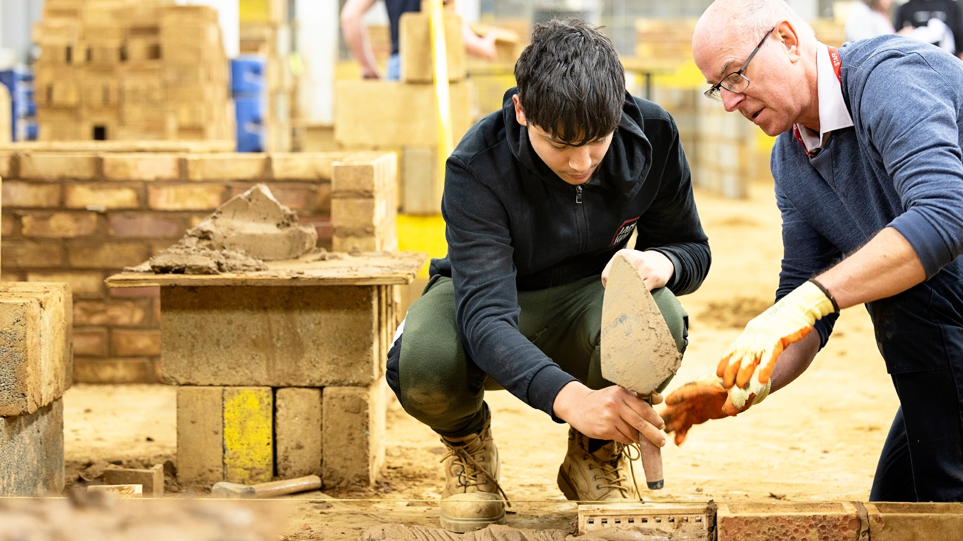 Two people working together applying mortar while laying bricks.