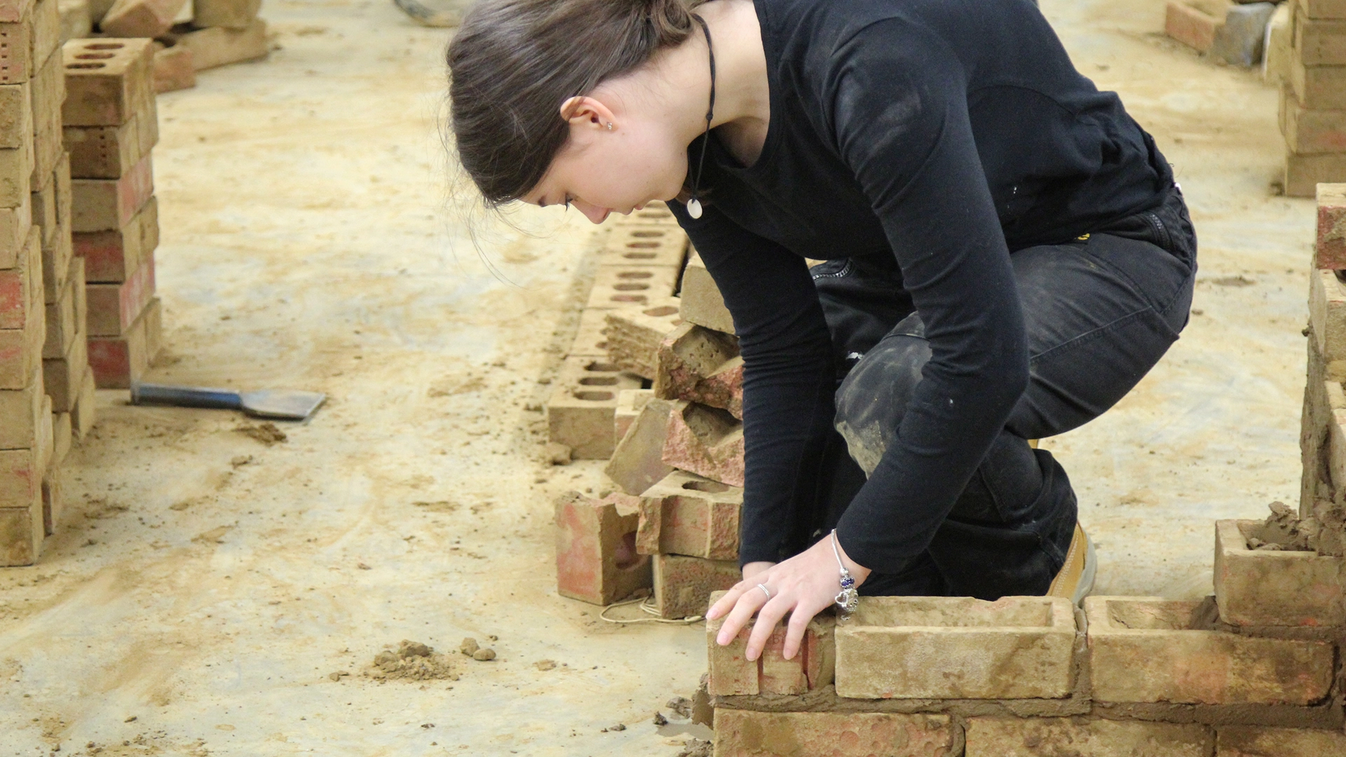 Person kneeling and positioning bricks on a construction training floor.