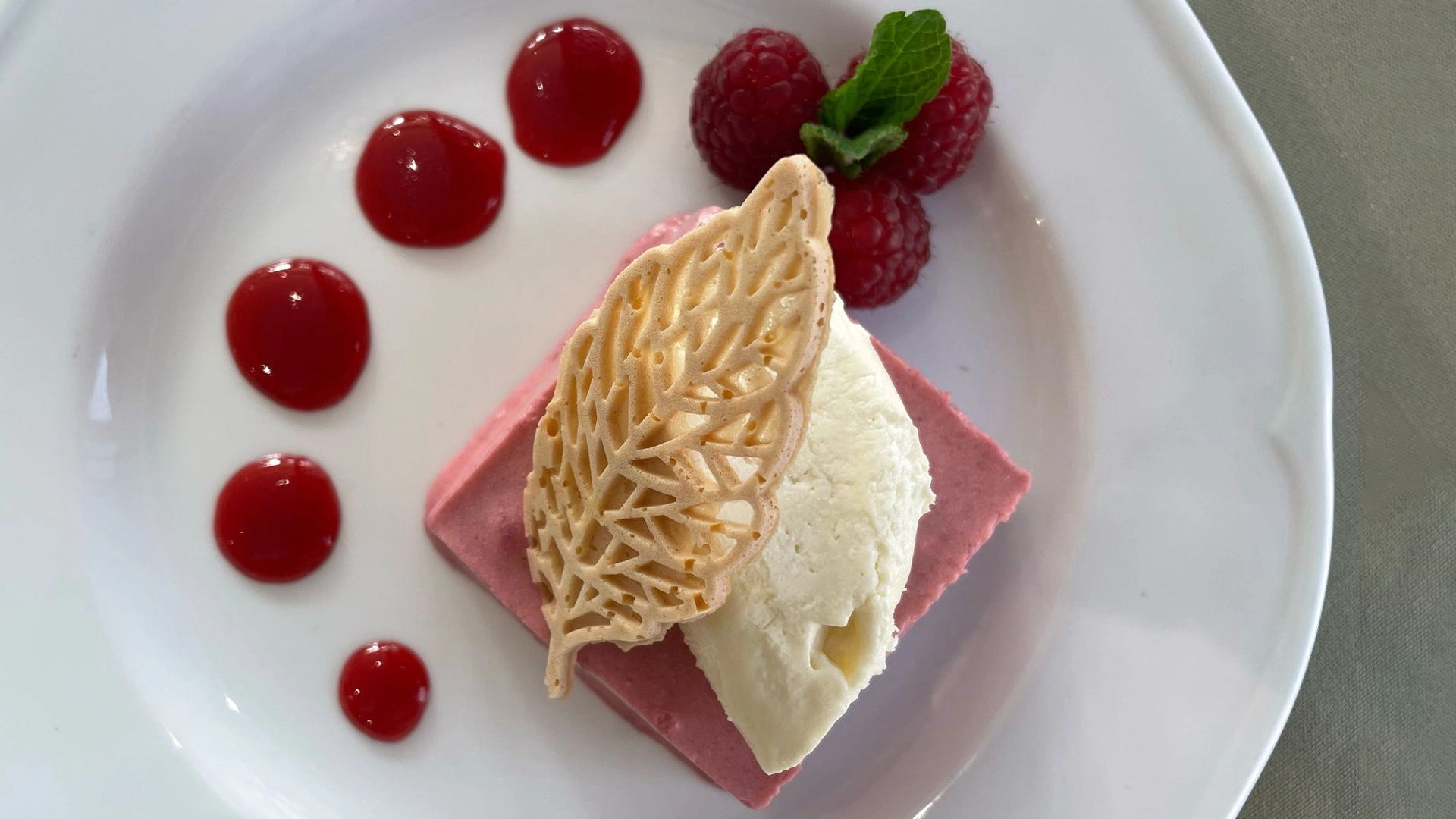 Plated dessert with raspberry mousse, vanilla ice cream, raspberries and red sauce dots.