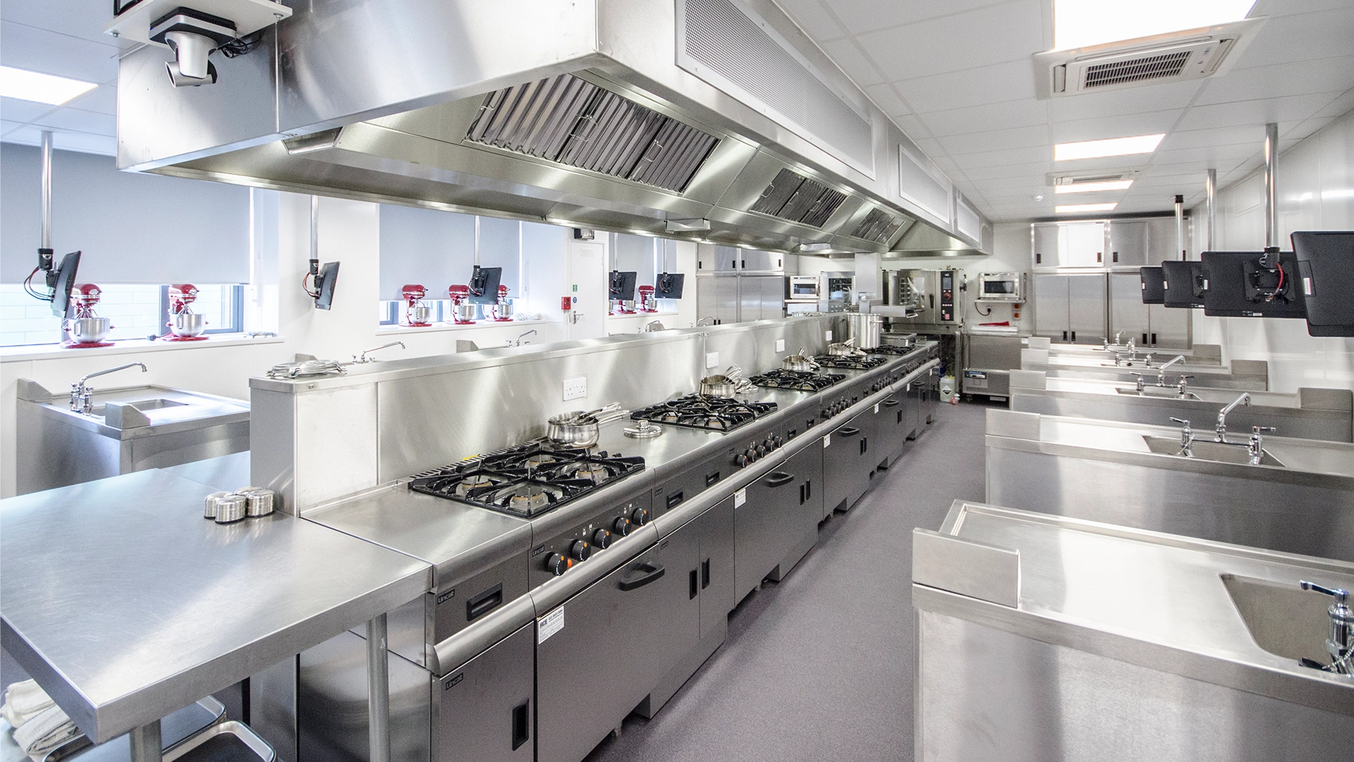 Wide view of a professional teaching kitchen with cooking stations and equipment.