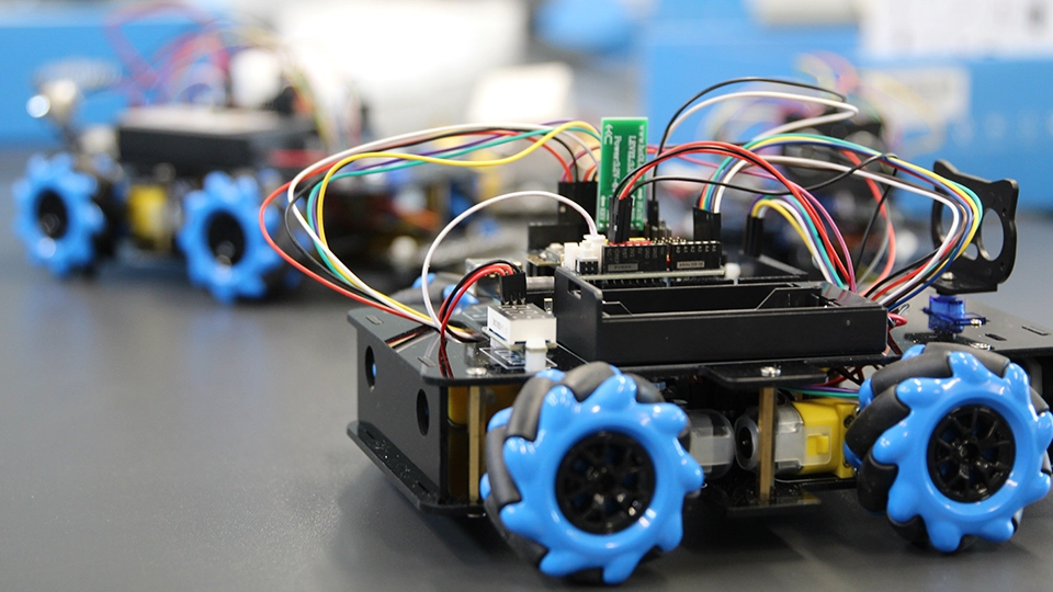 Four-wheeled robotics platform with exposed wiring and sensors on a work surface