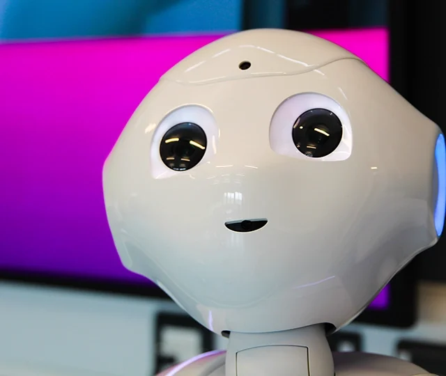 Close-up of humanoid robot head with lit eyes in front of a screen