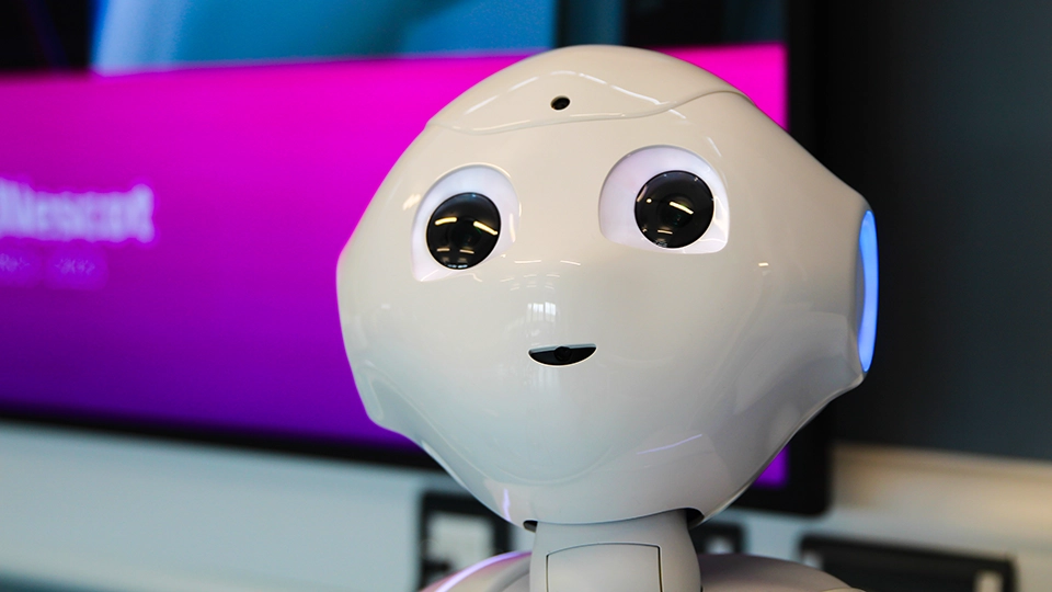 Close-up of humanoid robot head with lit eyes in front of a screen