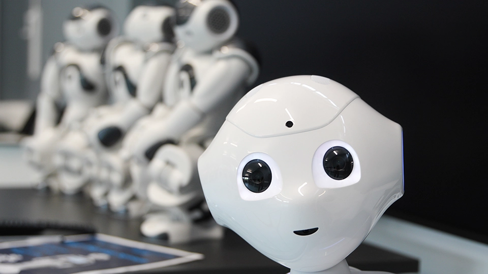 Humanoid robot in foreground with similar robots arranged behind on a table