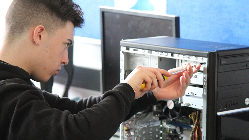 Student using a screwdriver to install or adjust hardware inside a desktop PC