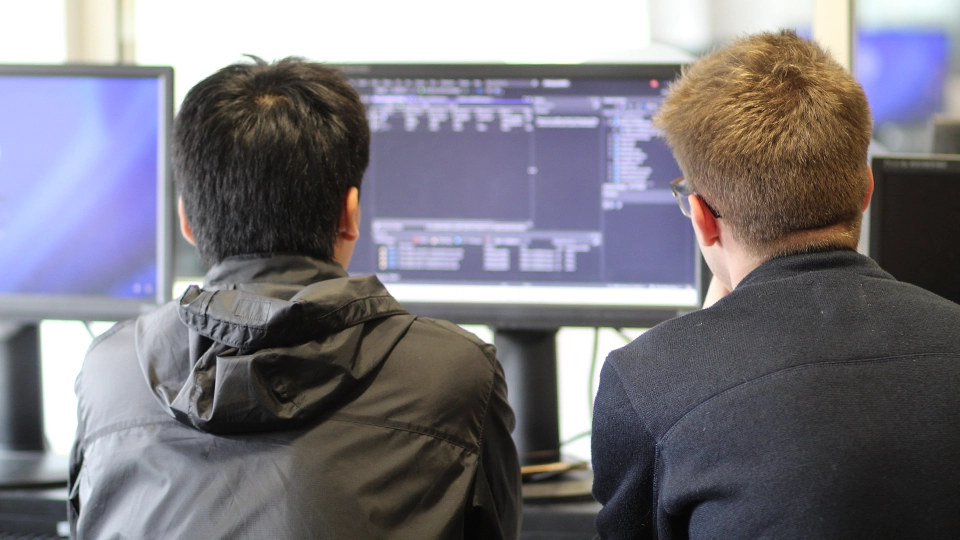 Two students viewing code on a desktop monitor in a computer lab