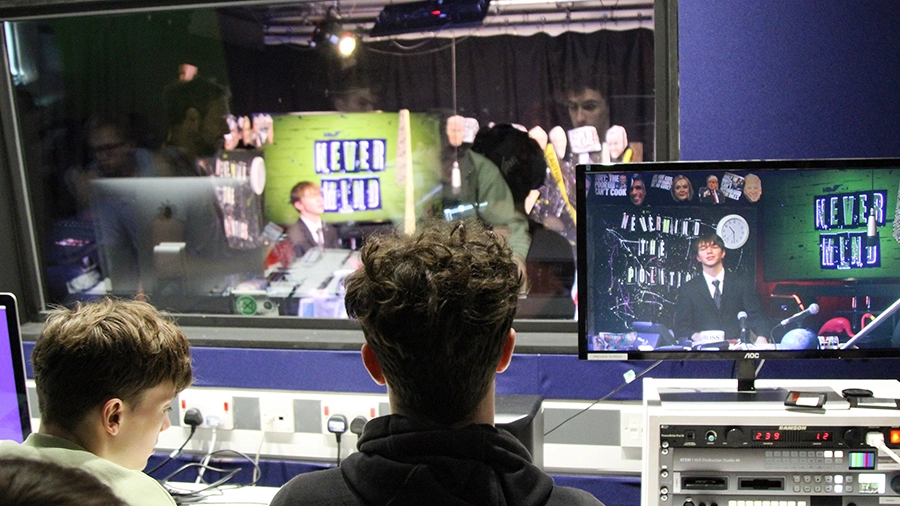 Students in a control room monitoring a live studio broadcast on screens.