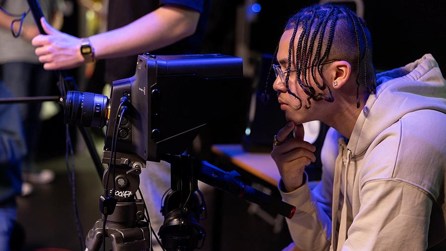 Student adjusting a camera on a tripod during a practical filming session.