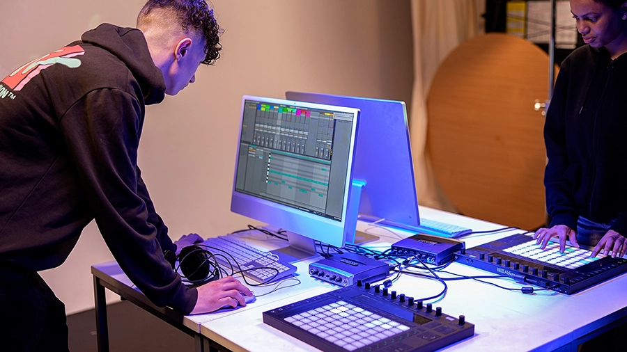 Students producing music on a computer with MIDI controllers and audio equipment.