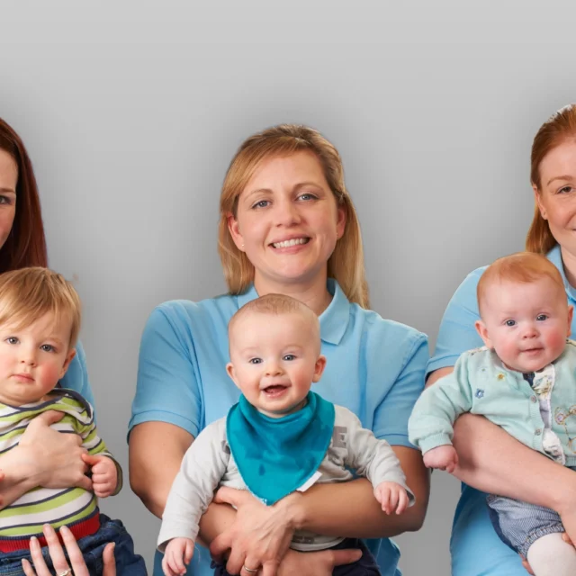 Three nursery staff in a classroom holding babies.