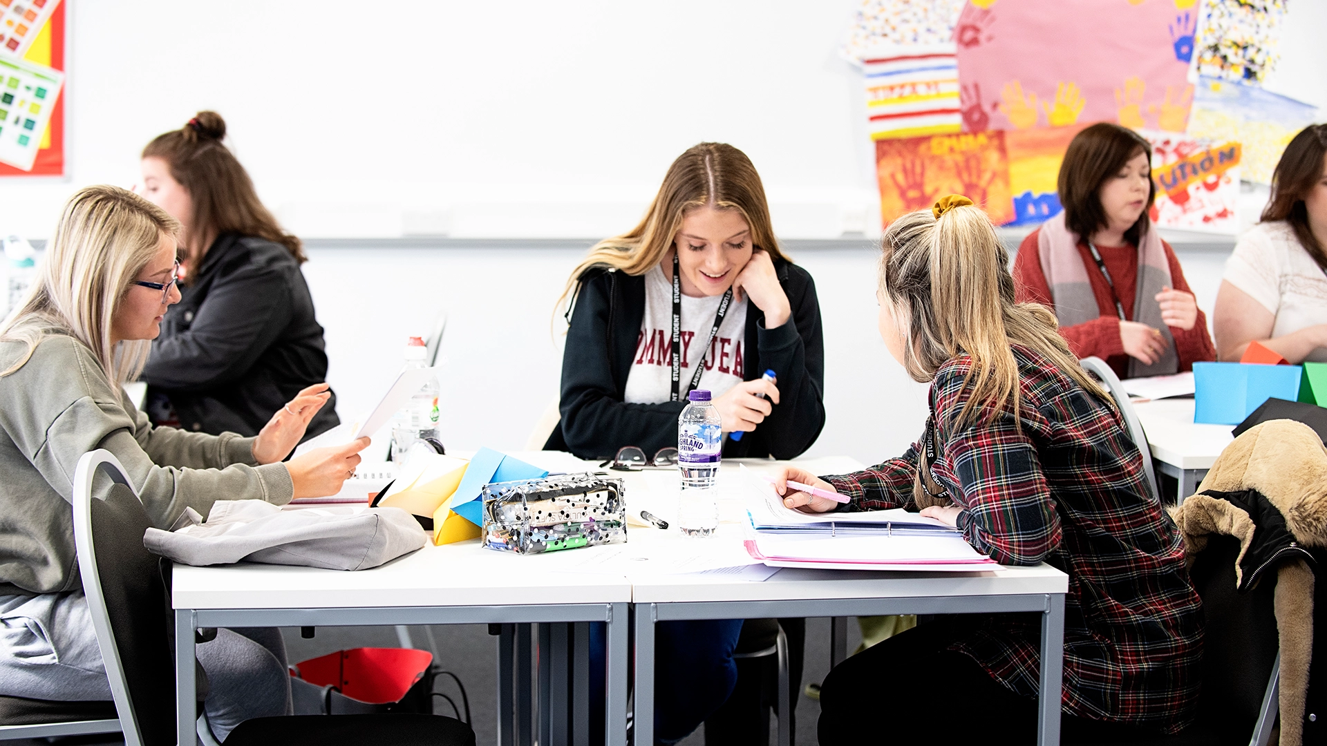 Students sitting at tables in a classroom, reading and discussing work.