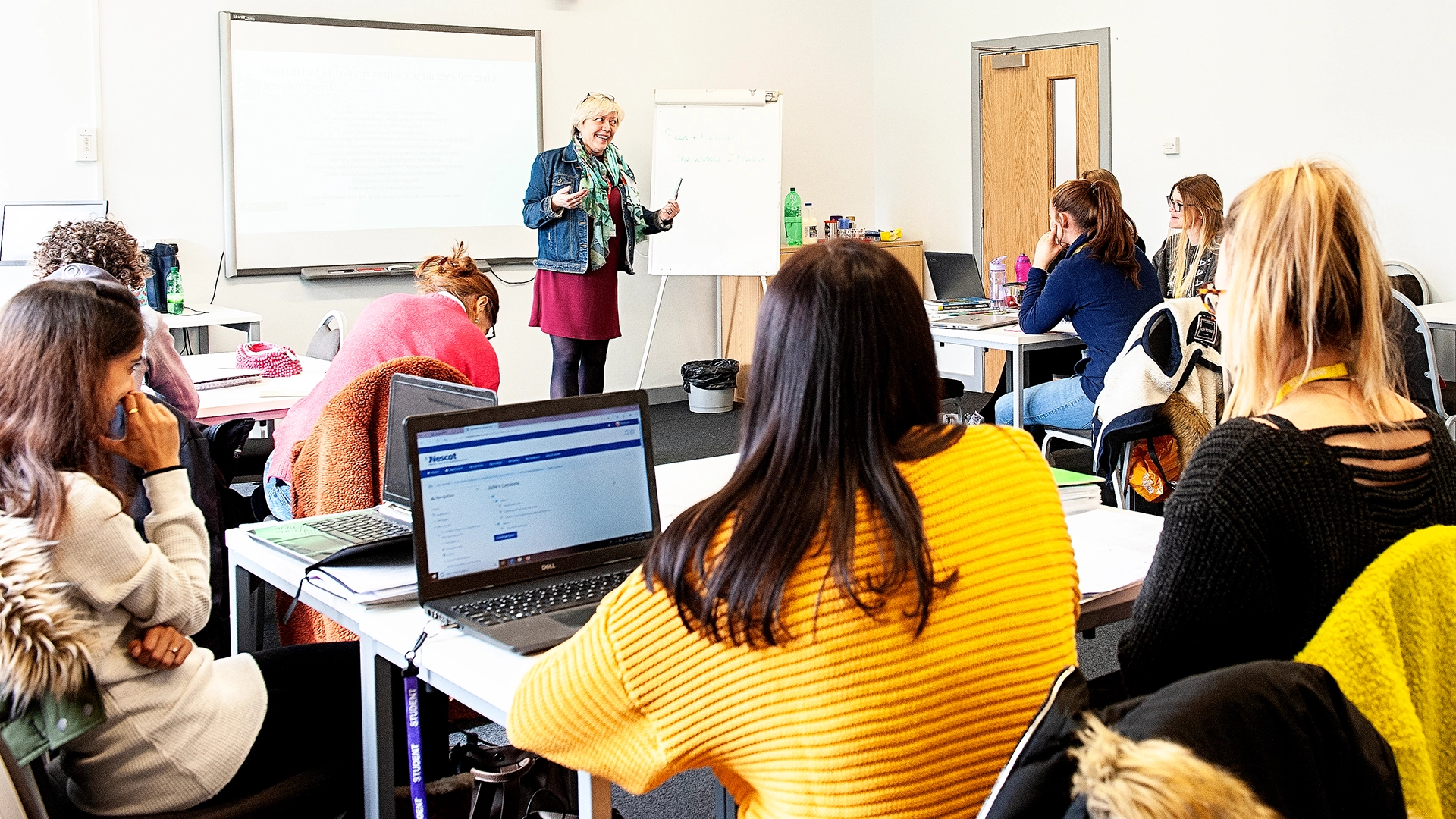 Tutor standing at the front of a classroom teaching a group of adult learners.
