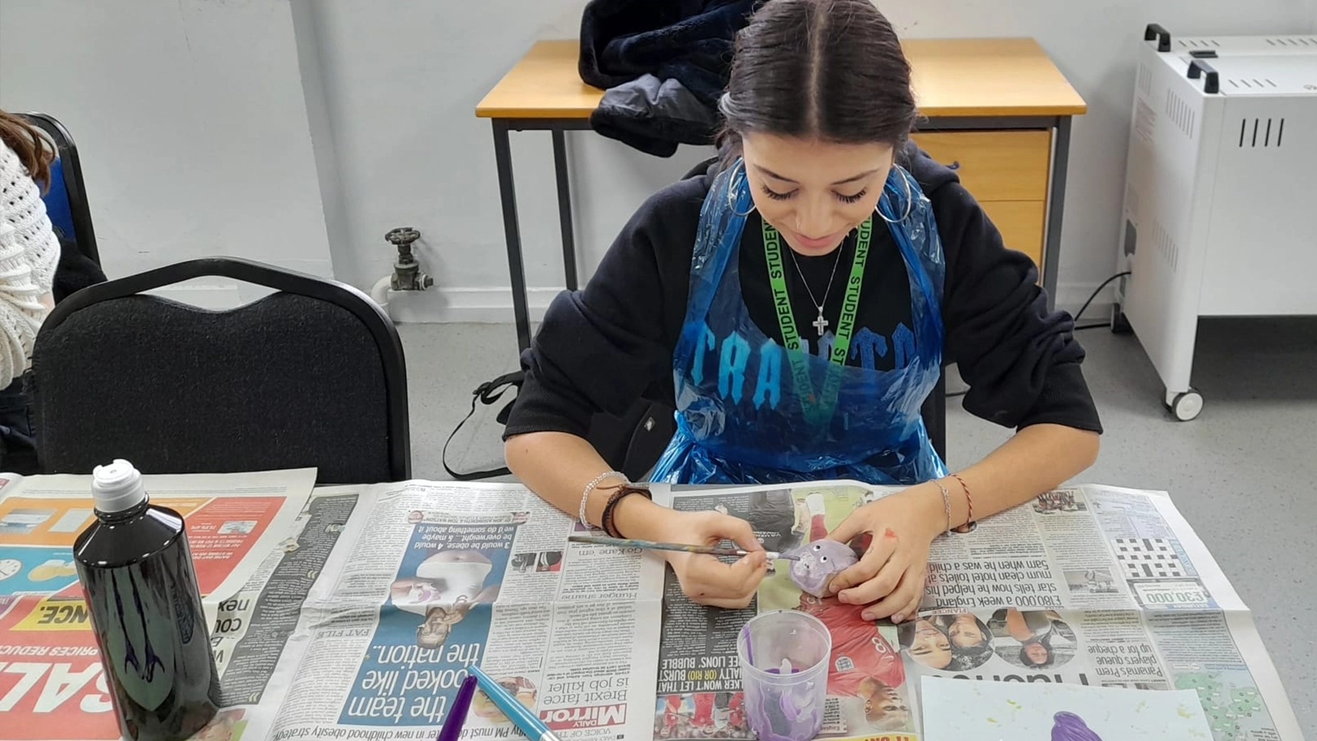 Student painting a small object at a desk covered with newspaper.