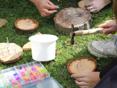 Hands using tools to hammer nails into wood outdoors on grass.