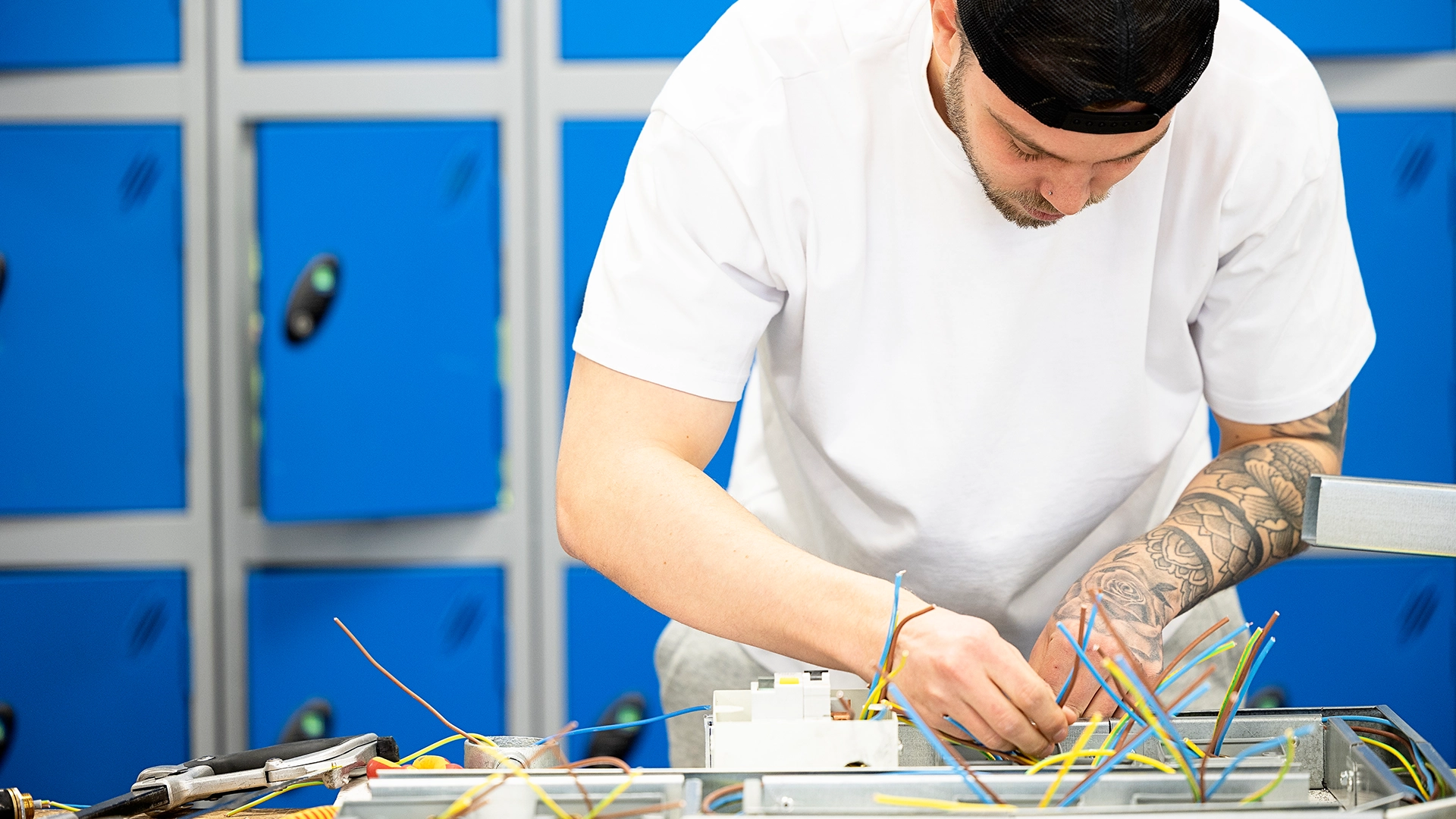 Apprentice connecting electrical wires inside a metal unit on a workbench
