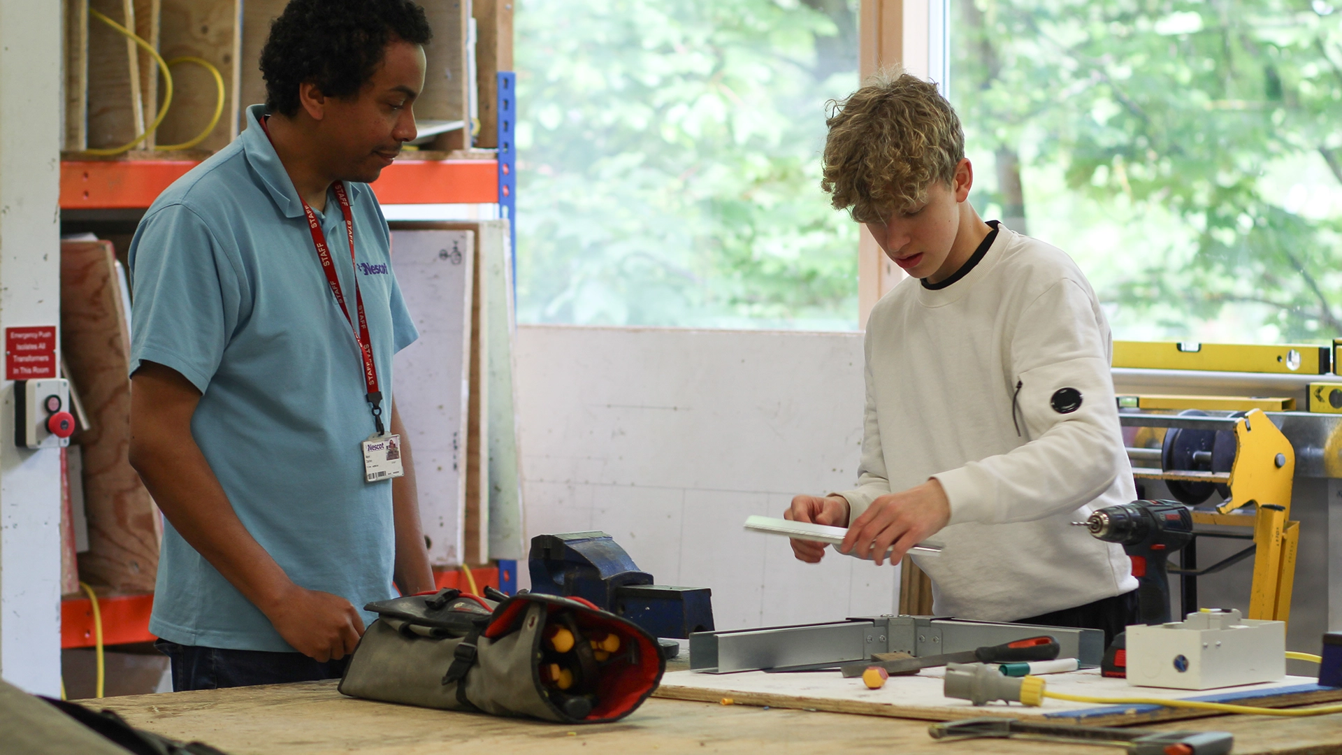 Learner measuring and assembling electrical components on a workbench with tutor support