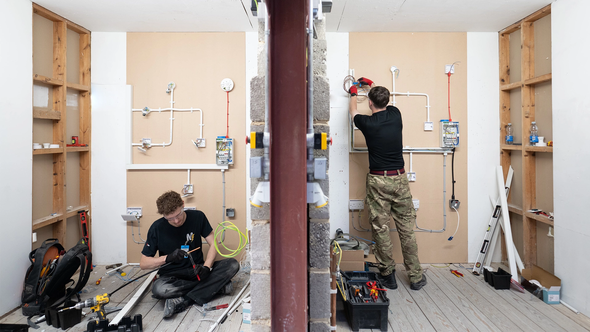 Two apprentices installing wiring and testing circuits in a training workshop