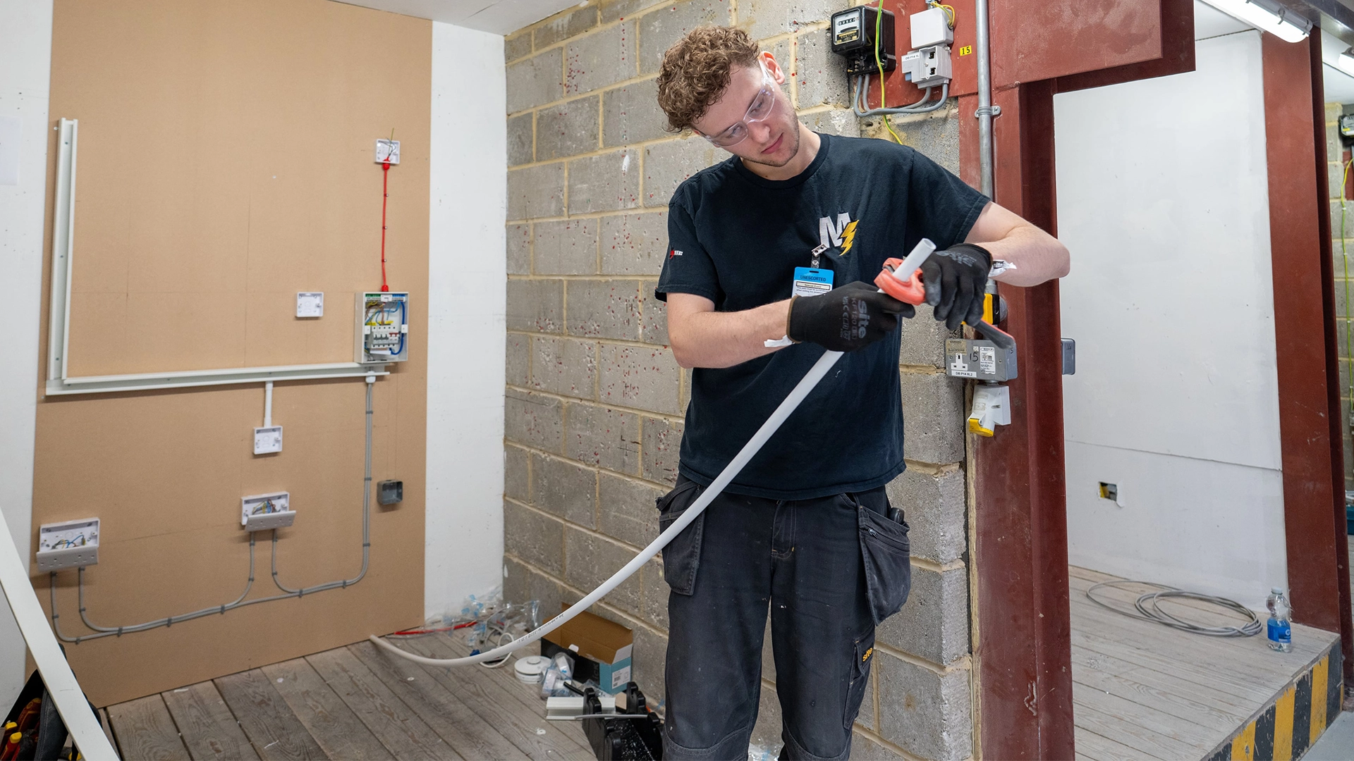 Apprentice cutting and fitting plastic conduit in an electrical training room