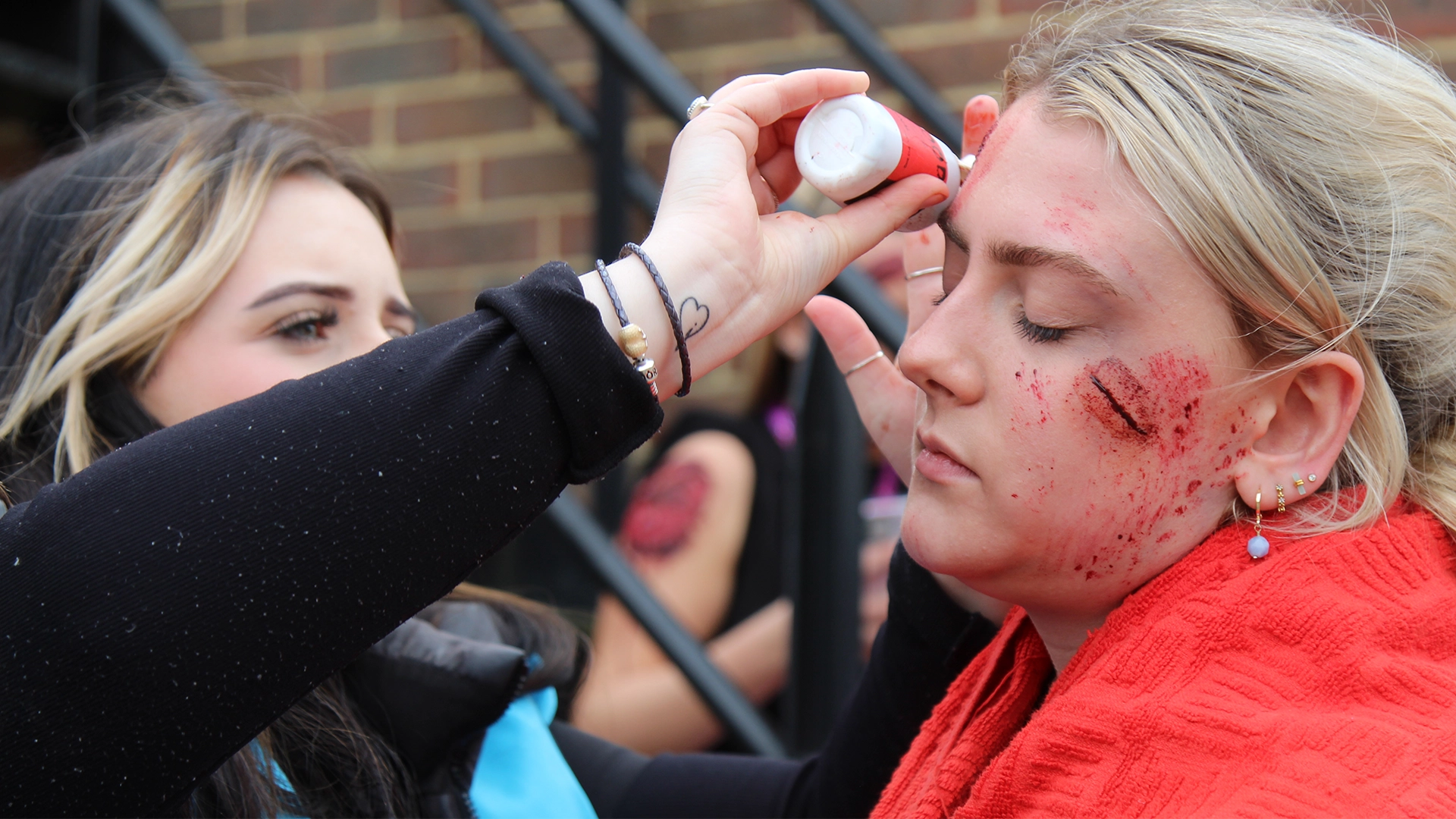 Student applying special effects make-up to create a realistic injury on an actor’s face.