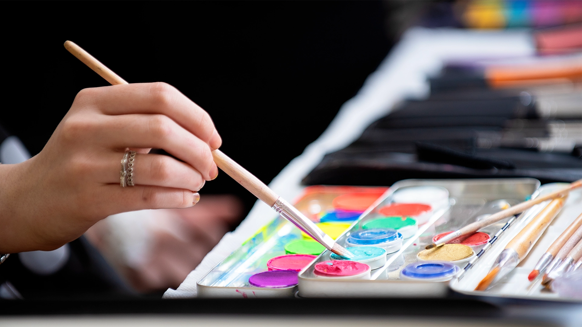 Close-up of a paintbrush being used on a palette of bright colours.