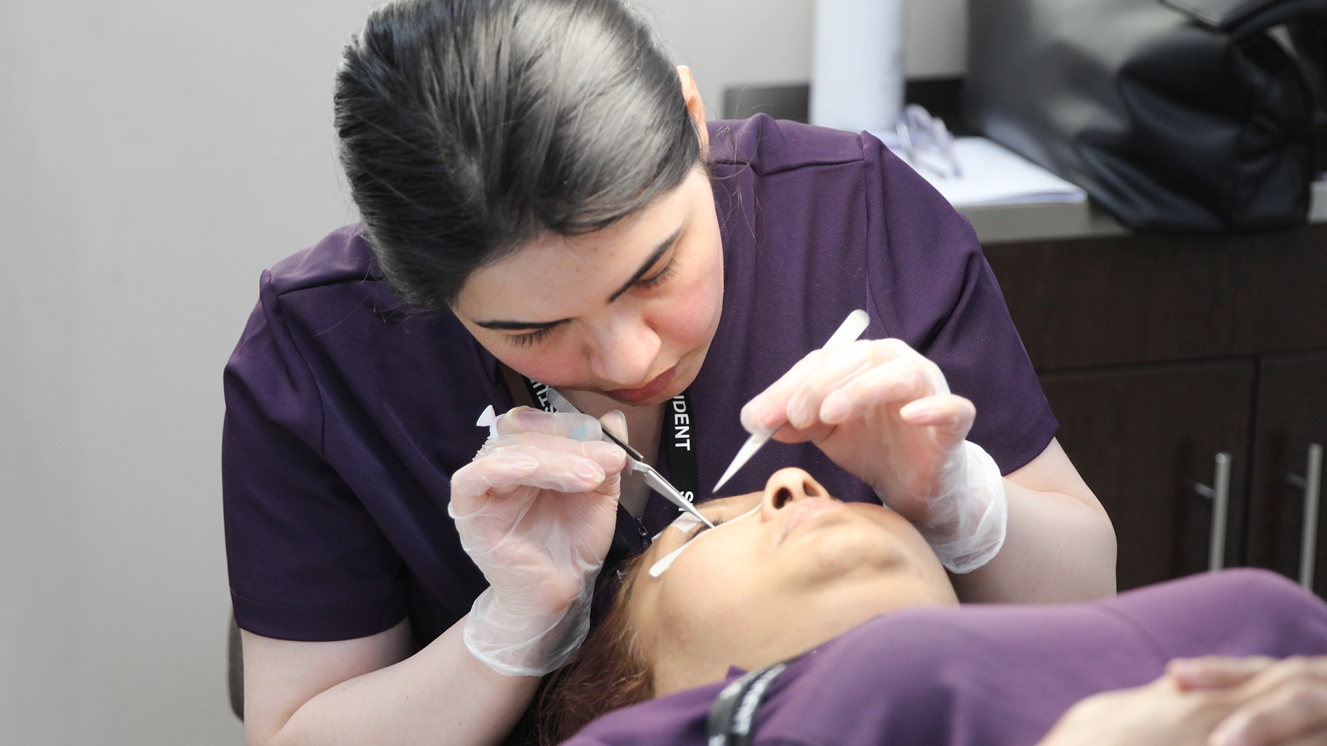 Close-up of a student performing an eye or lash treatment on a client.