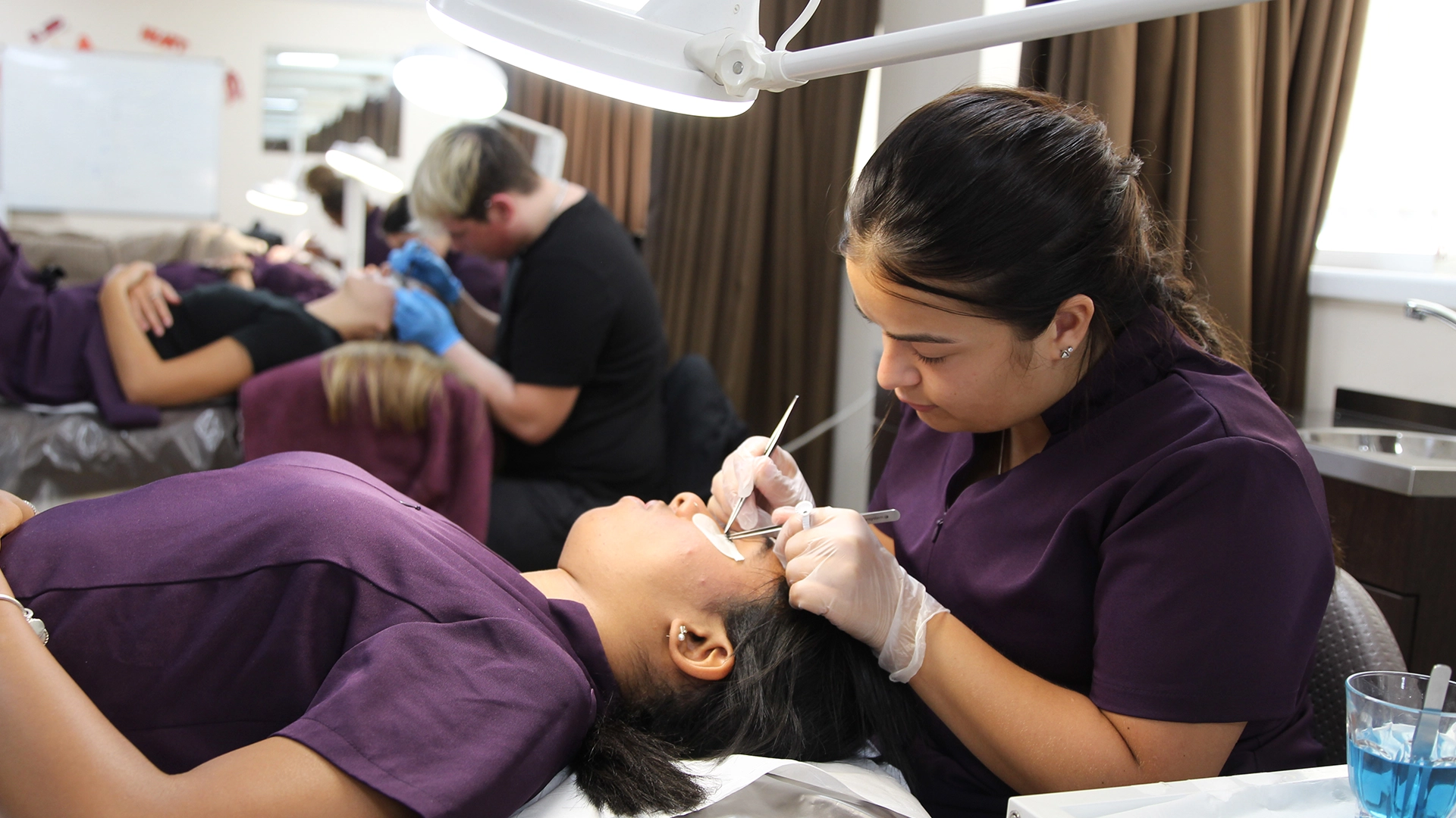 Student carrying out an eyelash treatment on a client in a salon training room.