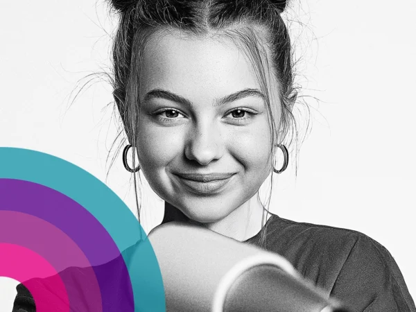 Portrait of a person with hair tied up and hoop earrings, facing the camera with one arm raised holding a hairdryer